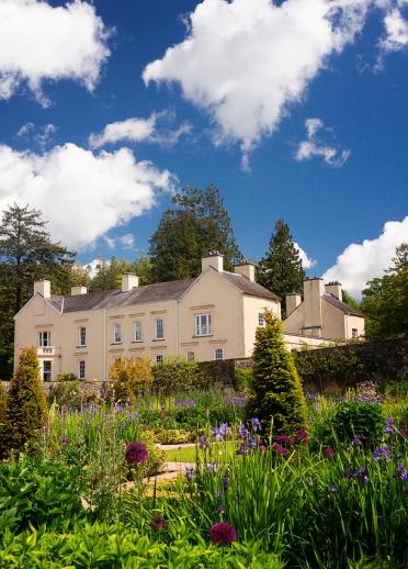 A grand house set in colourful gardens on a sunny day.