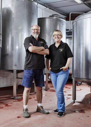 The owners of a brewery standing by large silver vats.