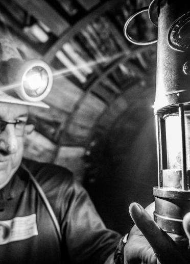 A black and white image of a former coal miner and his lamp down a pit.