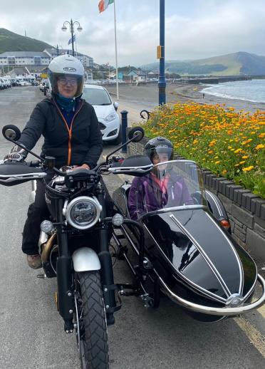 People in a motorcycle and sidecar with views of the coast beyond.