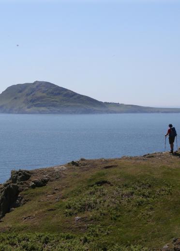 A view of Bardsey Island from the Welsh mainland, with a walker looking out to the island