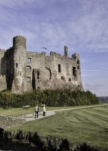 exterior of Laugharne castle with two people walking along footpath.