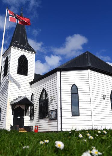 Die weiße Norwegian Church mit der norwegischen Flagge und Gras im Vordergrund.