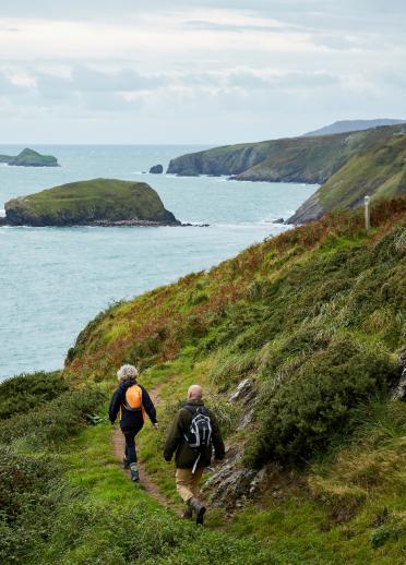 A man and a woman walking along the coast path with the sea on the left hand side