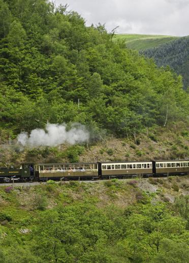 Steam train and its carriages travelling amongst the hills on the Vale of Rheidol Railway.