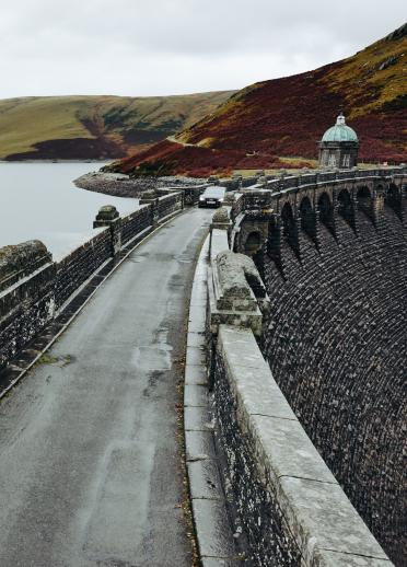 car driving on stone bridge with reservoir.