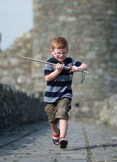 Little boy running through Harlech Castle with pretend wooden sword