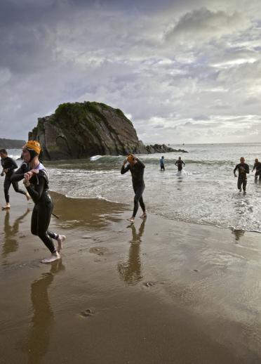 Competitors finishing swimming stage of Ironman Wales, running out of the sea onto North Beach, Tenby