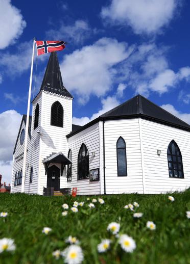 View of the Norwegian Church behind a lawn full of daisies.