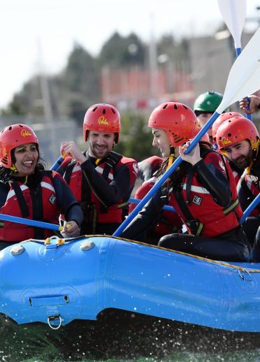 A group of people wearing helmets, wetsuits and life jackets in a white water rafting boat.