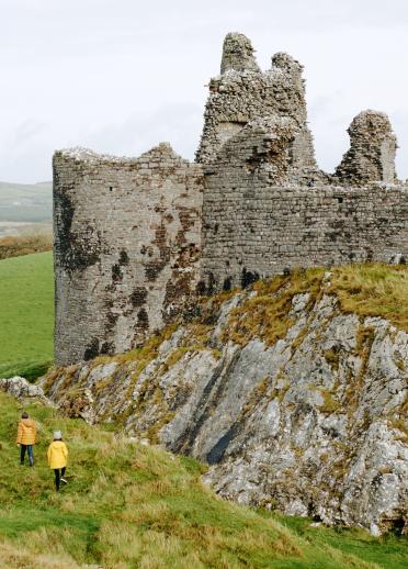 Two people exploring external stone walls of Carreg Cennen Castle.