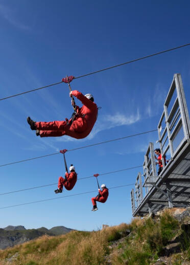 Three people sitting in a harness on parallel zip lines.