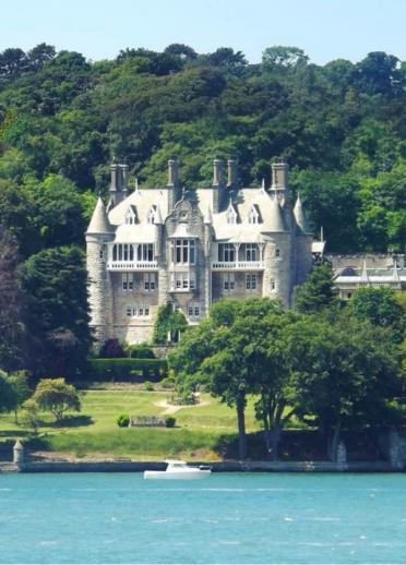 Exterior view of Chateau Rhianfa from across water, surrounded by green trees. 