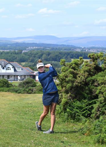 Lady golfer after taking a swing with the clubhouse and views of mountains in the background.
