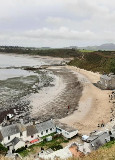 A panoramic view of Porthdinllaen headland with houses and the Ty Coch Inn in the forefront and mountains in the background.