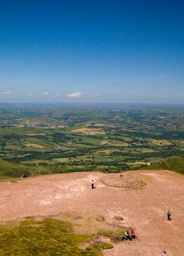Aerial view of the green plains below from the top of Pen y Fan with blue skies.