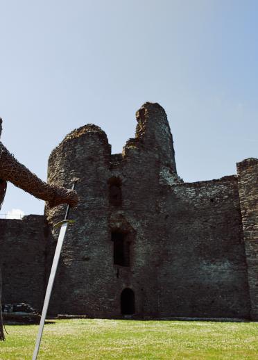 lifesize wicker figure of soldier with sword in foreground and castle ruins in background.