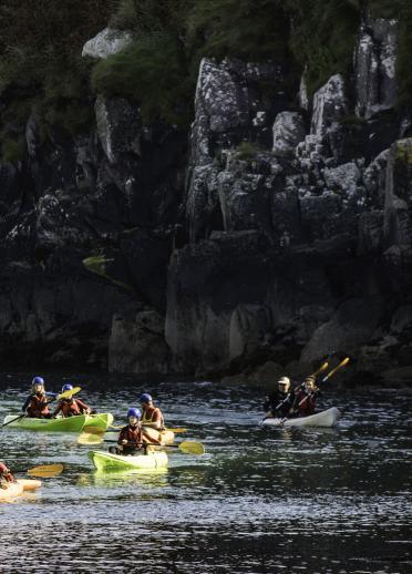 several people kayaking, with cliff face in background.