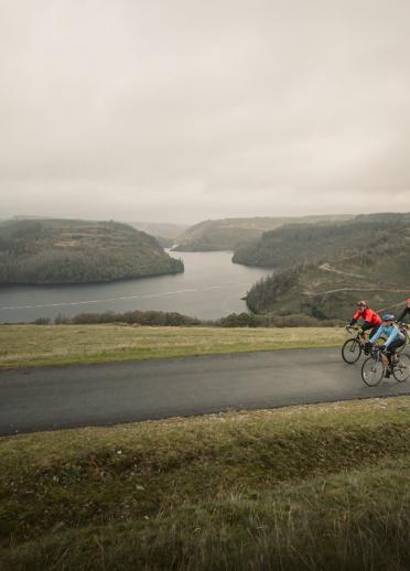 A group cycling on a narrow road above a lake.