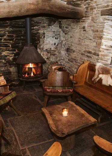 room with stone tiled floor, wooden furniture and fur rug, white brick walls and wood burning fire.