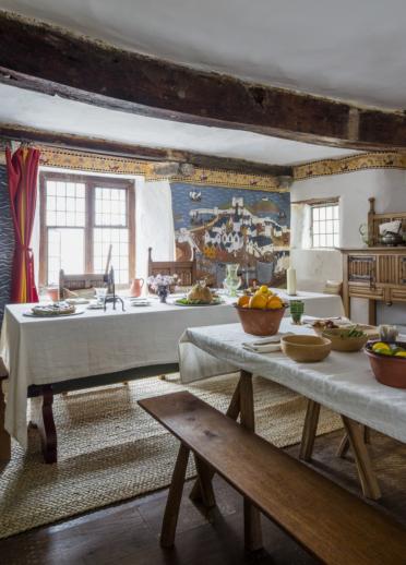 interior of 15th century room with decorative walls and laid tables with white clothes and benches