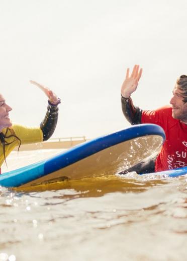 2 people on a surfboard doing a high five.