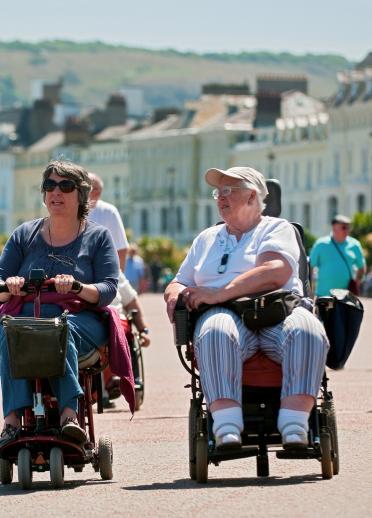 Two women using a wheelchair and mobility scooter on the promenade