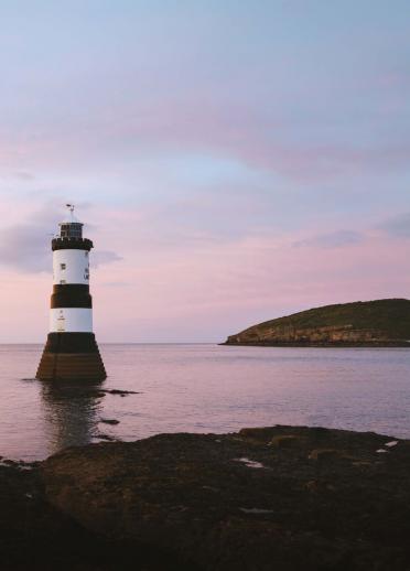 Lighthouse with pale pink sky and water.