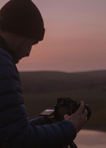 Seitenansicht eines Mannes im Freien bei schwachem Licht, der auf die Rückseite einer Kamera blickt.