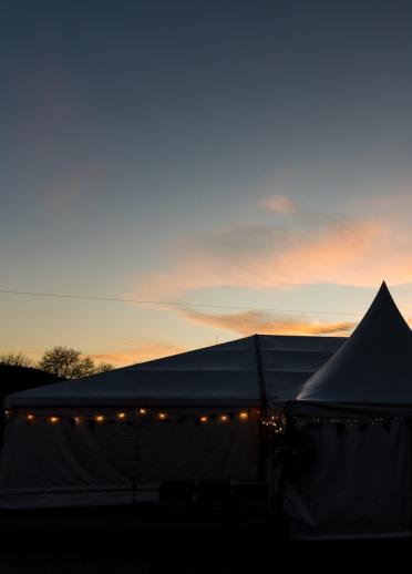 A festival marquee at the Hay Winter festival weekend, with a string of lights around it, against a dusk sky.