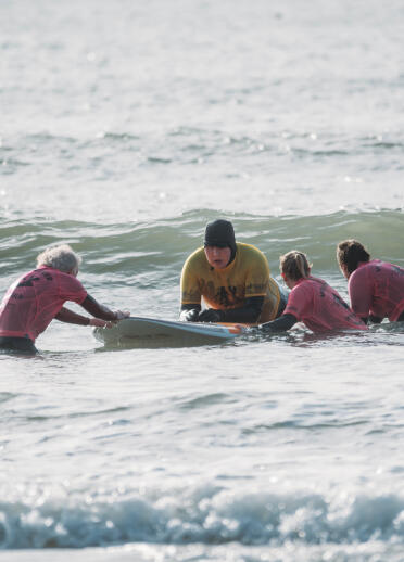 A man on a surfboard with a group of people helping. 