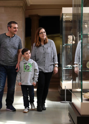 A family of three looking at artefacts in a glass cabinet.