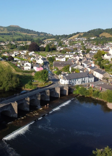 Aerial view of a town with an arched stone bridge over a wide river in the foreground.