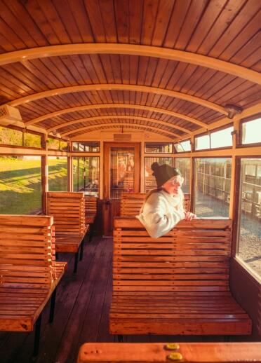 Das hölzerne, sitzende Innere eines Wagens einer historischen Eisenbahn mit einem Fahrgast, der aus dem Fenster schaut.