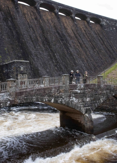 Eine Steinbrücke mit Menschen darauf, unter einem Damm.