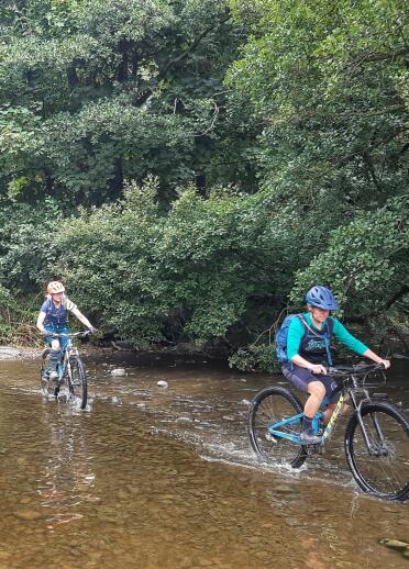 Two women on mountain bikes riding through a stream.