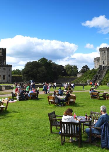 People sat on tables and chairs in the grounds of Cardiff Castle.