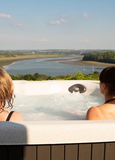 Two people sat in a hot tub looking out at a view over a river.