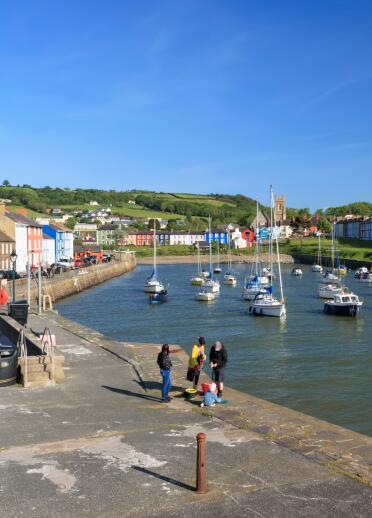 A town harbour with moored sailing boats and a family crabbing off the harbourside.