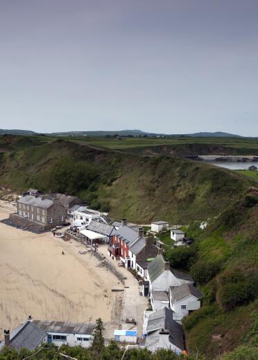 Image of buildings on the beach, backing onto green hills.