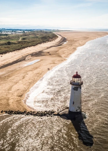 Aerial view of a lighthouse on a wide, sandy beach.