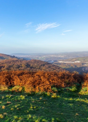 Ausblick von einem Berg auf eine Stadt und grüne Hügel im Hintergrund.