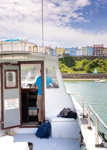 two men fishing from a boat on a sunny day with colourful buildings of Tenby in the distance.