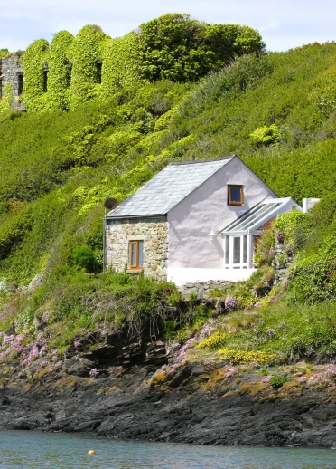 Ein kleines Steinhaus oberhalb der Wasserlinie umgeben von grüner Küste
