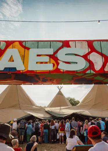 Sign reading 'Maes b' with festival tents and people.