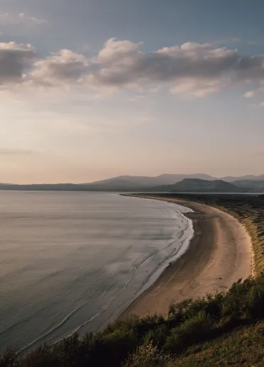 A long sandy beach with dunes and mountains in the background.