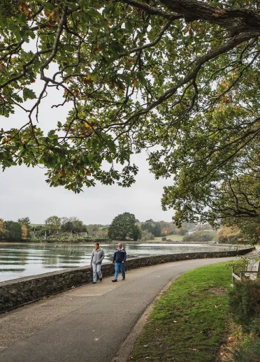 Two adults and a dog walking along a waterside path. 