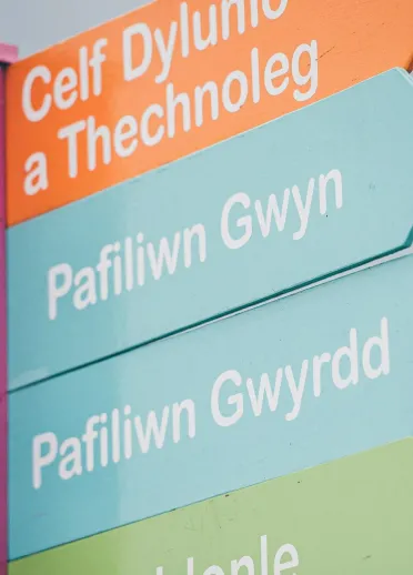 Colourful signpost with arrow-shaped boards pointing in different directions, labelled Cardiff Bay, Tenby Beach, Pembrokeshire Coast and Brecon Beacons.