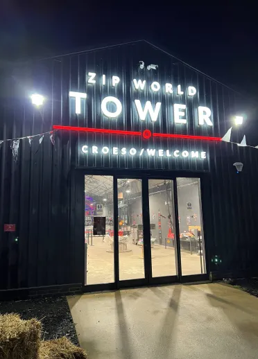 Night-time view of a glass-fronted entrance with illuminated Tower sign and lit interior visible through the doors.