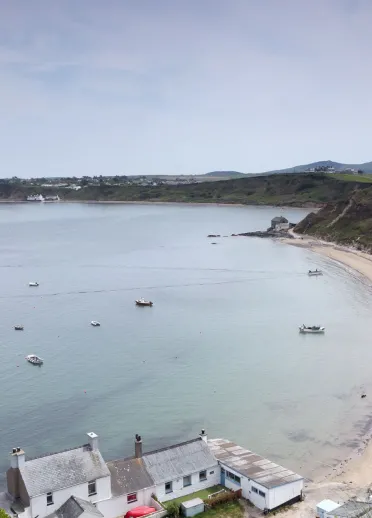 High up view over a curved sandy beach with clear blue waters, with buildings along the cliff edge.